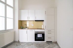 A compact kitchen with white cabinets, a black oven, and a window providing natural light. - 2-bedroom apartment with elevator | Naschmarkt | Sleeps 6 (Wien)