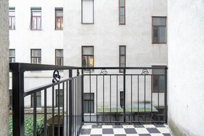 A balcony with a black and white checkered floor, a metal railing, and a building with multiple windows in the background. - 2-bedroom apartment with elevator | Naschmarkt | Sleeps 6 (Wien)