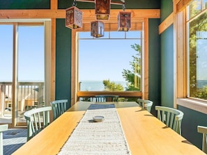 Un comedor con una mesa de madera, sillas y vista al océano a través de amplios ventanales.