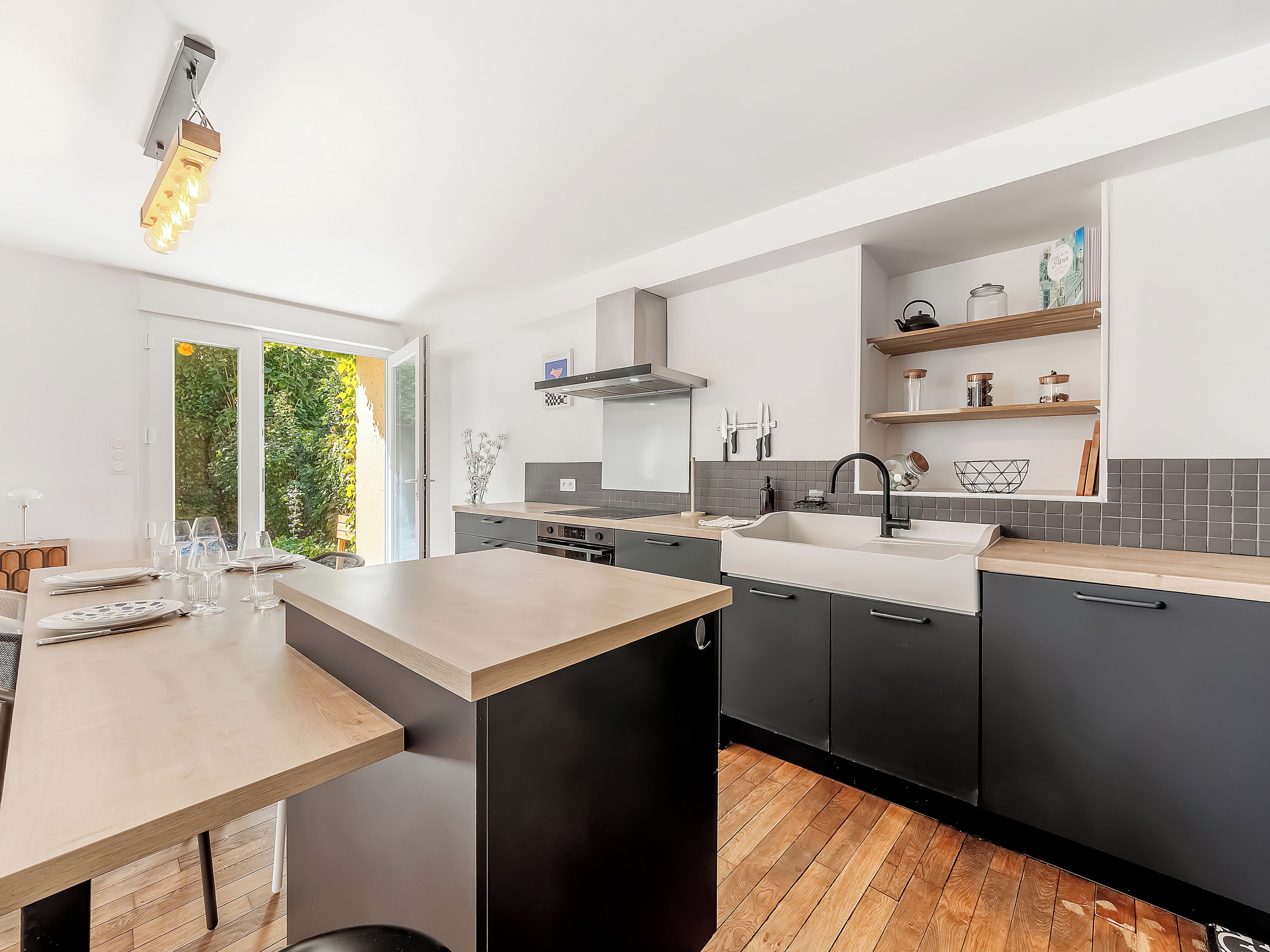 Une cuisine moderne dotée d’un îlot central, de meubles de couleur sombre et offrant une vue sur la verdure environnante.