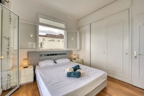 A bedroom with a bed, bedside tables, a wardrobe, and a window with a view of buildings. - Gasparin - Vue mer - Climatisation (Saint-Denis)