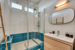 A modern bathroom with a glass-enclosed shower, a vanity with a mirror, and a blue accent wall. - Gasparin - Vue mer - Climatisation (Saint-Denis)
