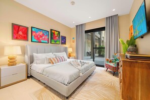A hotel room with a large bed, a flat-screen TV, a desk with a lamp, and artwork on the walls. - 2BR Luxury Escape | Pool, Palapa & Outdoor Shower (Noord)