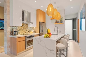 A modern kitchen with a marble island, stainless steel appliances, and a hanging wicker light fixture. - 2BR Luxury Escape | Pool, Palapa & Outdoor Shower (Noord)