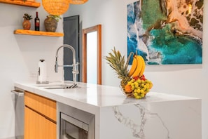 A kitchen with a marble countertop, a modern faucet, and a fruit bowl with bananas, grapes, and a pineapple. - 2BR Luxury Escape | Pool, Palapa & Outdoor Shower (Noord)