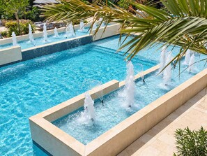 A rectangular pool with multiple water jets, surrounded by a tiled deck and palm trees. - 2BR Luxury Escape | Pool, Palapa & Outdoor Shower (Noord)