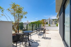 A rooftop terrace with a table and chairs, a potted tree, and a view of the cityscape. - Well-located Studio in Condo. Pti0505 (Florianópolis)