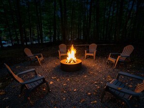 A campfire with four Adirondack chairs arranged around it in a forest setting. - Welcome to the "Cozy Hideout" Charming 3/3 home in the Lake Ariel community. (Lake Ariel)
