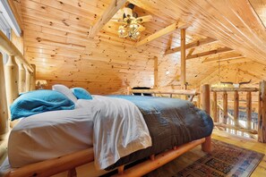 A wooden cabin interior with a bed, a chandelier, and a view of the outdoors. - Lake and Trailside Ranch Log Cabin (Augusta)