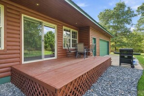 A wooden cabin with a covered deck, large windows, and a green garage door. - Lake and Trailside Ranch Log Cabin (Augusta)