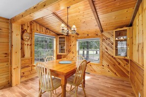 A wooden interior with a dining table, chairs, a chandelier, and large windows. - Lake and Trailside Ranch Log Cabin (Augusta)