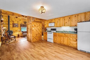 A wooden interior with a kitchen area featuring cabinets, a stove, a microwave, and a refrigerator. - Lake and Trailside Ranch Log Cabin (Augusta)