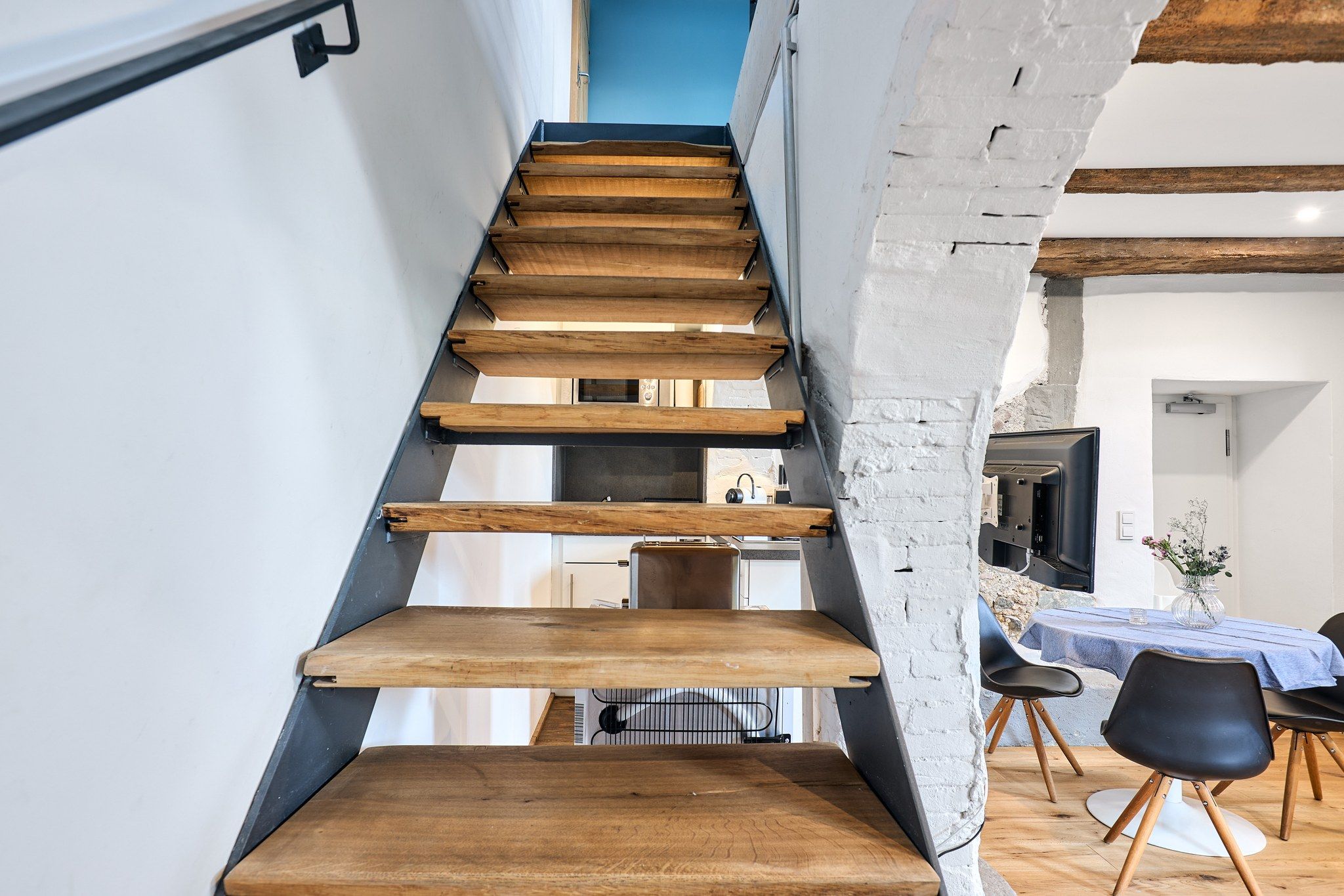 Una escalera de madera con diseño moderno que conduce a un comedor con mesa y sillas.