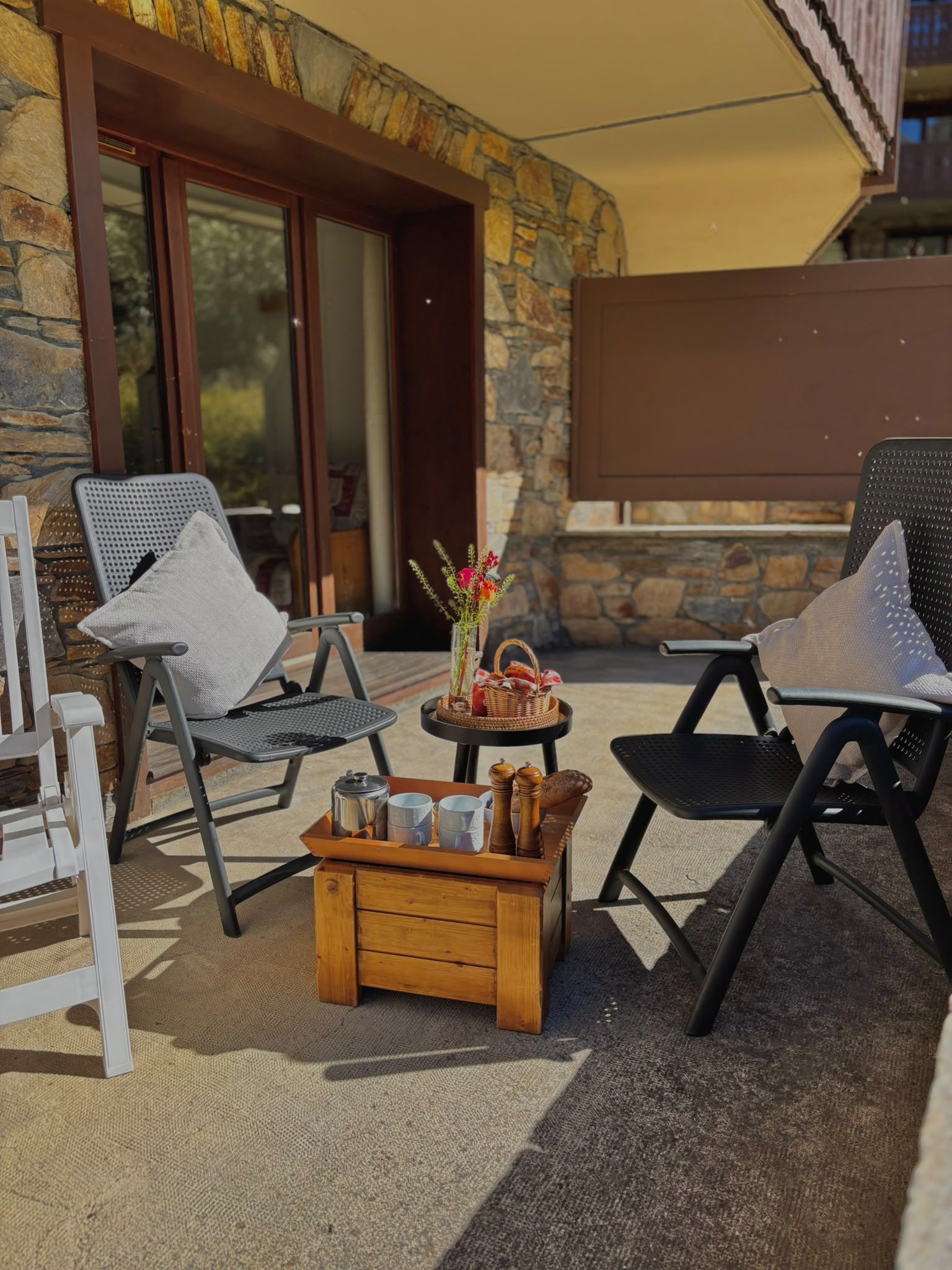 Un espace extérieur aménagé avec deux chaises, une petite table sur laquelle se trouve un plateau contenant divers objets, et un mur de pierre en arrière-plan.