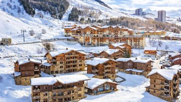 A snow-covered resort with multiple wooden buildings, ski lifts, and a mountainous backdrop.
