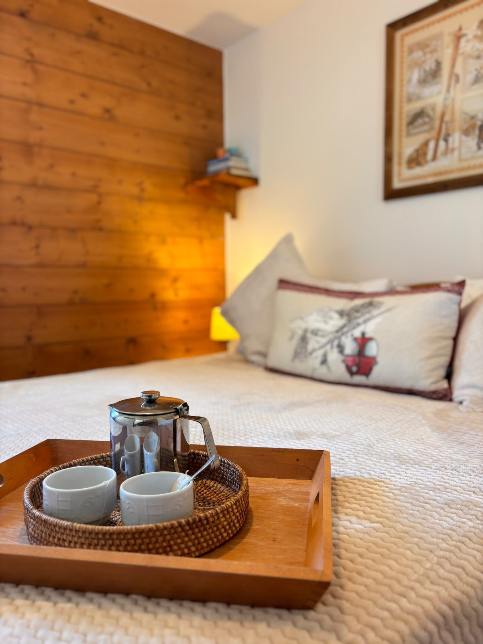 Ein Holztablett mit Teekanne und zwei Tassen auf einer gemusterten Tagesdecke.