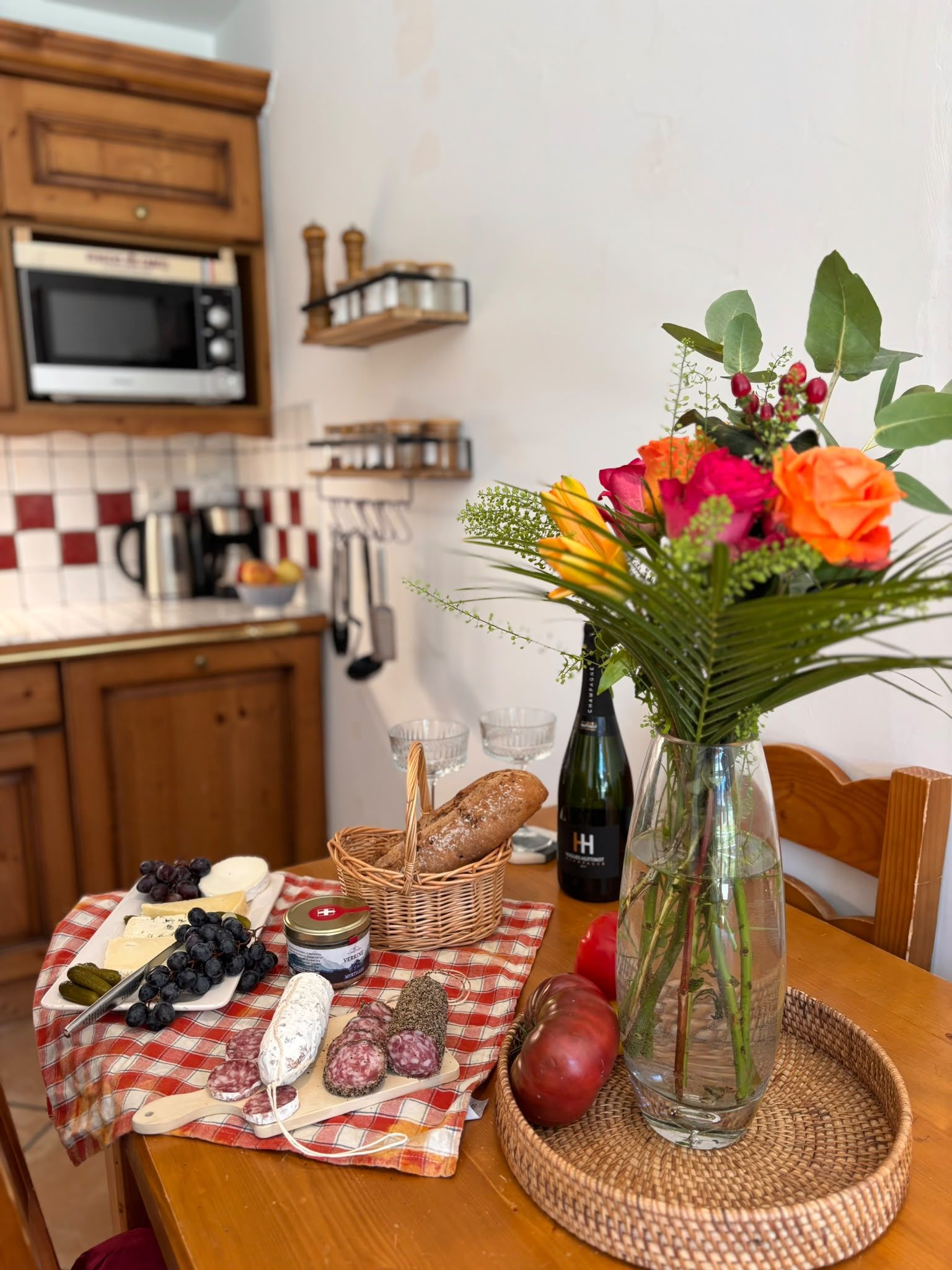 A kitchen counter with a variety of food items, a vase with flowers, and a bottle of champagne.