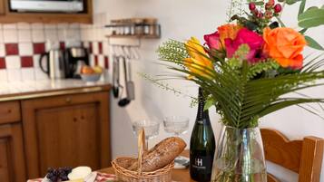 A kitchen counter with a variety of food items, a vase with flowers, and a bottle of champagne.