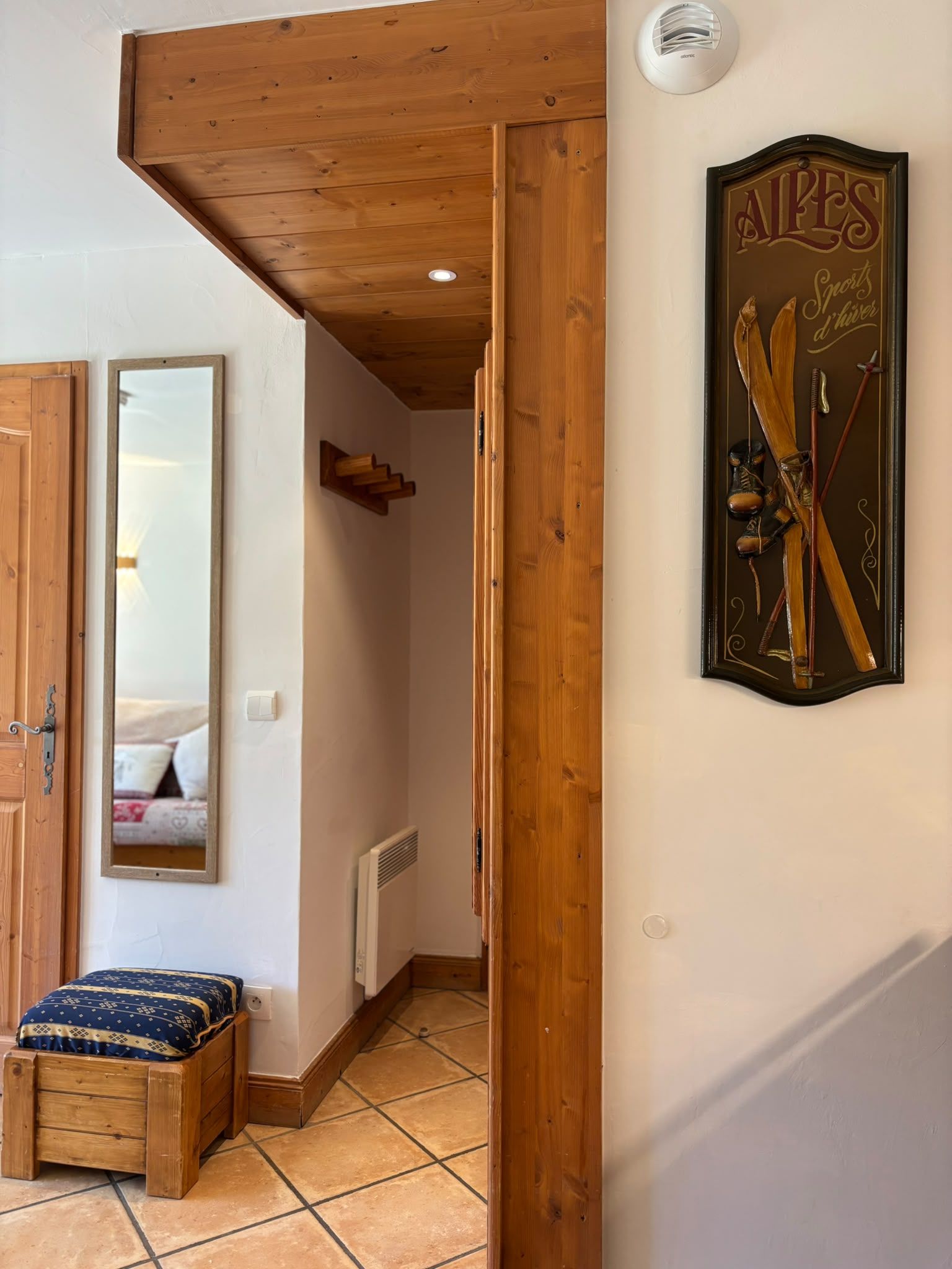 Un intérieur en bois avec un tableau encadré représentant du matériel de ski, un miroir et un petit banc.