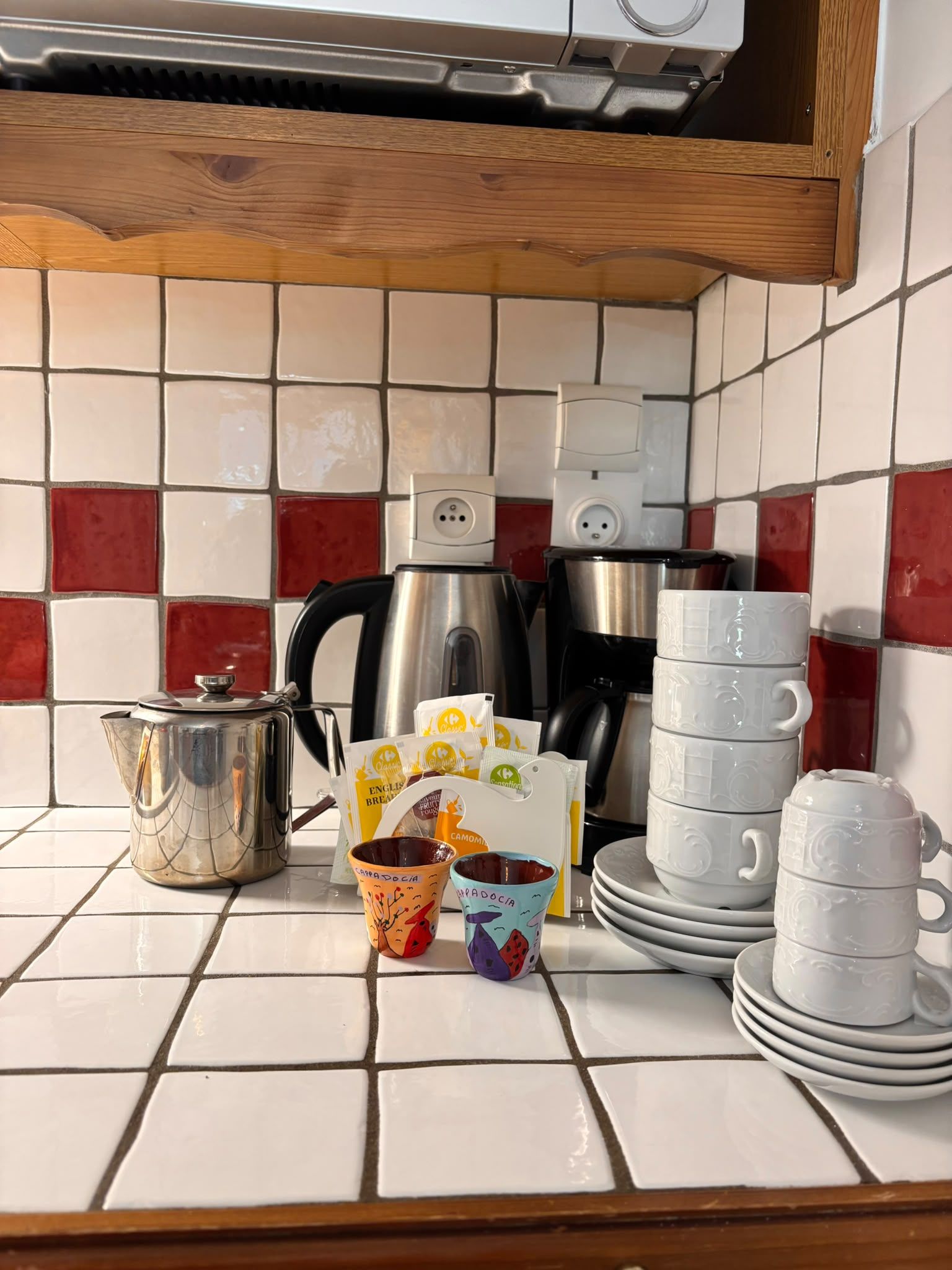A kitchen counter with a kettle, coffee maker, and various mugs and teacups.