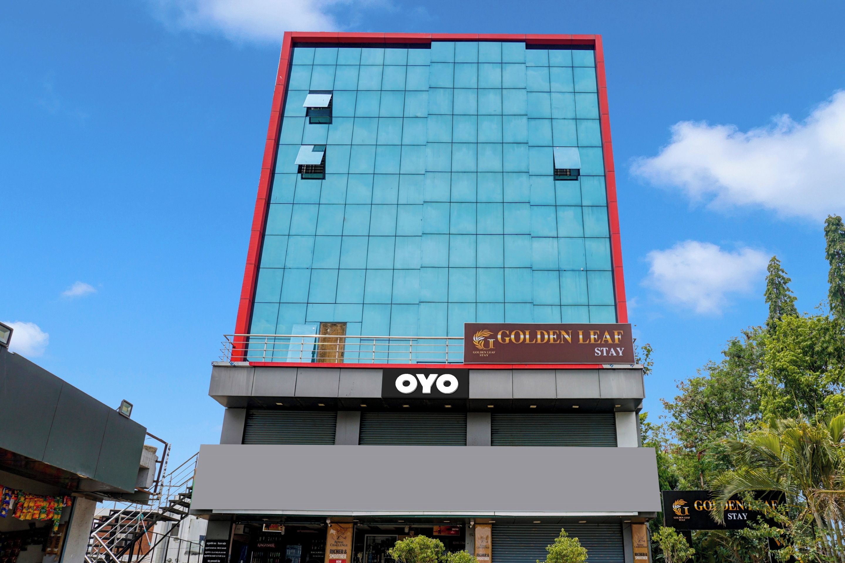 Un hotel con fachada moderna de vidrio, un letrero que dice 'Golden Leaf Stay' y la marca 'OVO' en la parte baja.