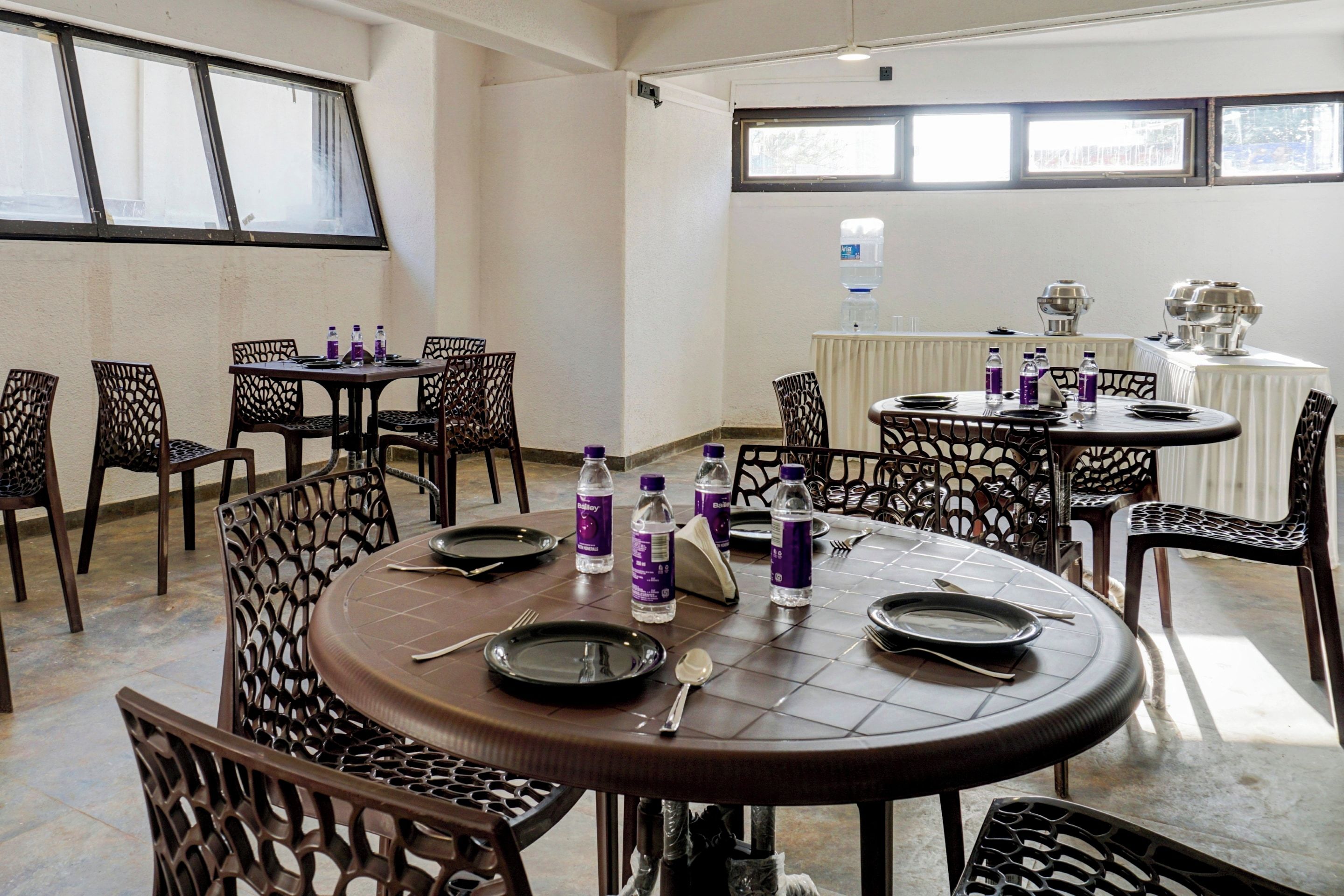 Un comedor con mesas y sillas redondas, botellas de agua y una parrilla sobre una mesa.