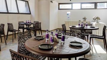 Un comedor con mesas y sillas redondas, botellas de agua y una parrilla sobre una mesa.