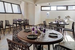 Un comedor con mesas y sillas redondas, botellas de agua y una parrilla sobre una mesa.