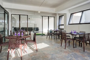 Amplio espacio interior con varias mesas y sillas, ventanas grandes y un ventanal de vidrio que da a un área exterior.