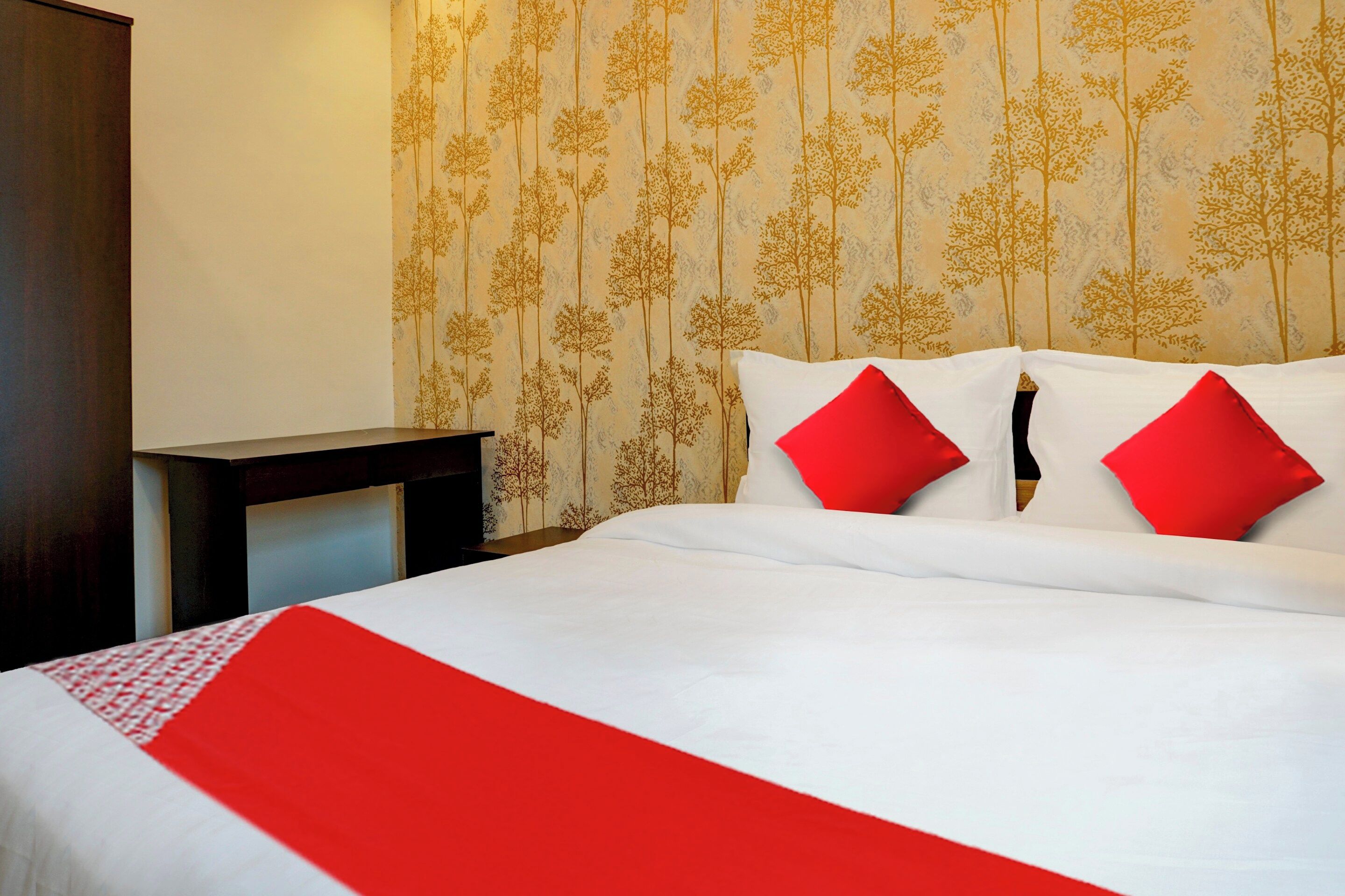 A hotel room with a bed, two red pillows, a white bedspread, and a red runner.