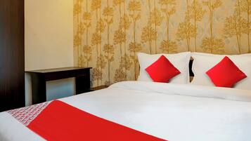 A hotel room with a bed, two red pillows, a white bedspread, and a red runner.