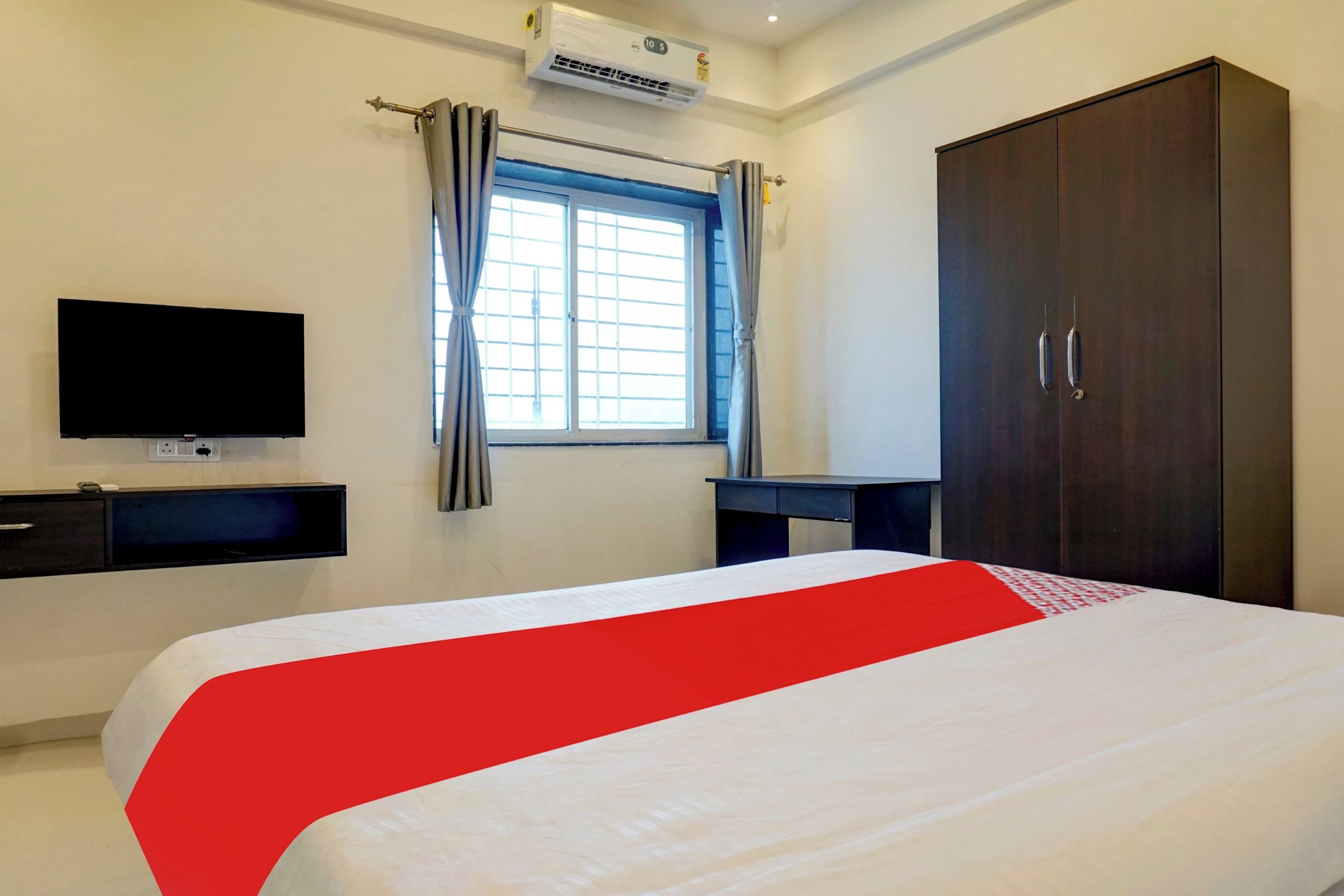 A hotel room with a bed, a TV, a wardrobe, and a window with curtains.