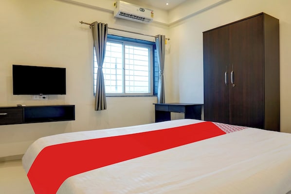 A hotel room with a bed, a TV, a wardrobe, and a window with curtains.