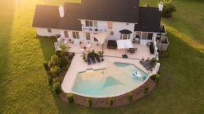 A large house with a swimming pool, outdoor seating, and a well-maintained lawn.