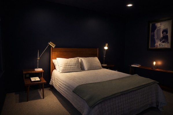 A hotel room with a large bed, two bedside tables, a nightstand, a framed picture on the wall, and a carpeted floor.