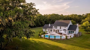 A large house with a swimming pool, surrounded by a well-maintained lawn and trees.
