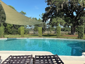A clear swimming pool with lounge chairs and a shaded area.