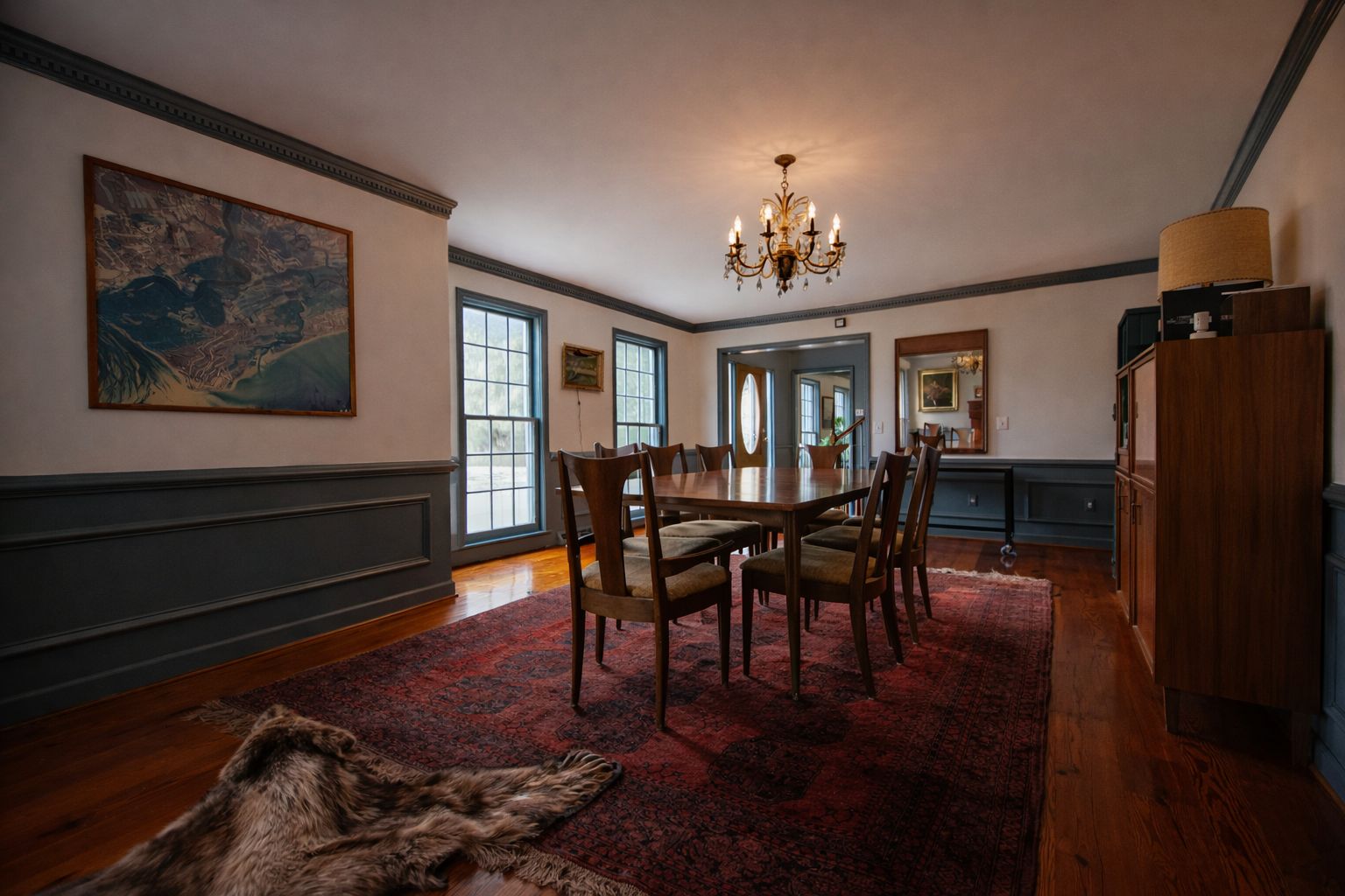 A dining room with a large table, chairs, a chandelier, and a fur rug on the floor.