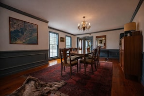 A dining room with a large table, chairs, a chandelier, and a fur rug on the floor.