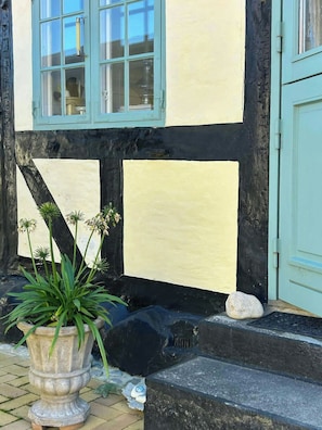 Ein Fachwerkhäuschen mit blauer Tür und Fenstern, einem Blumentopf und einer Steinstufe.