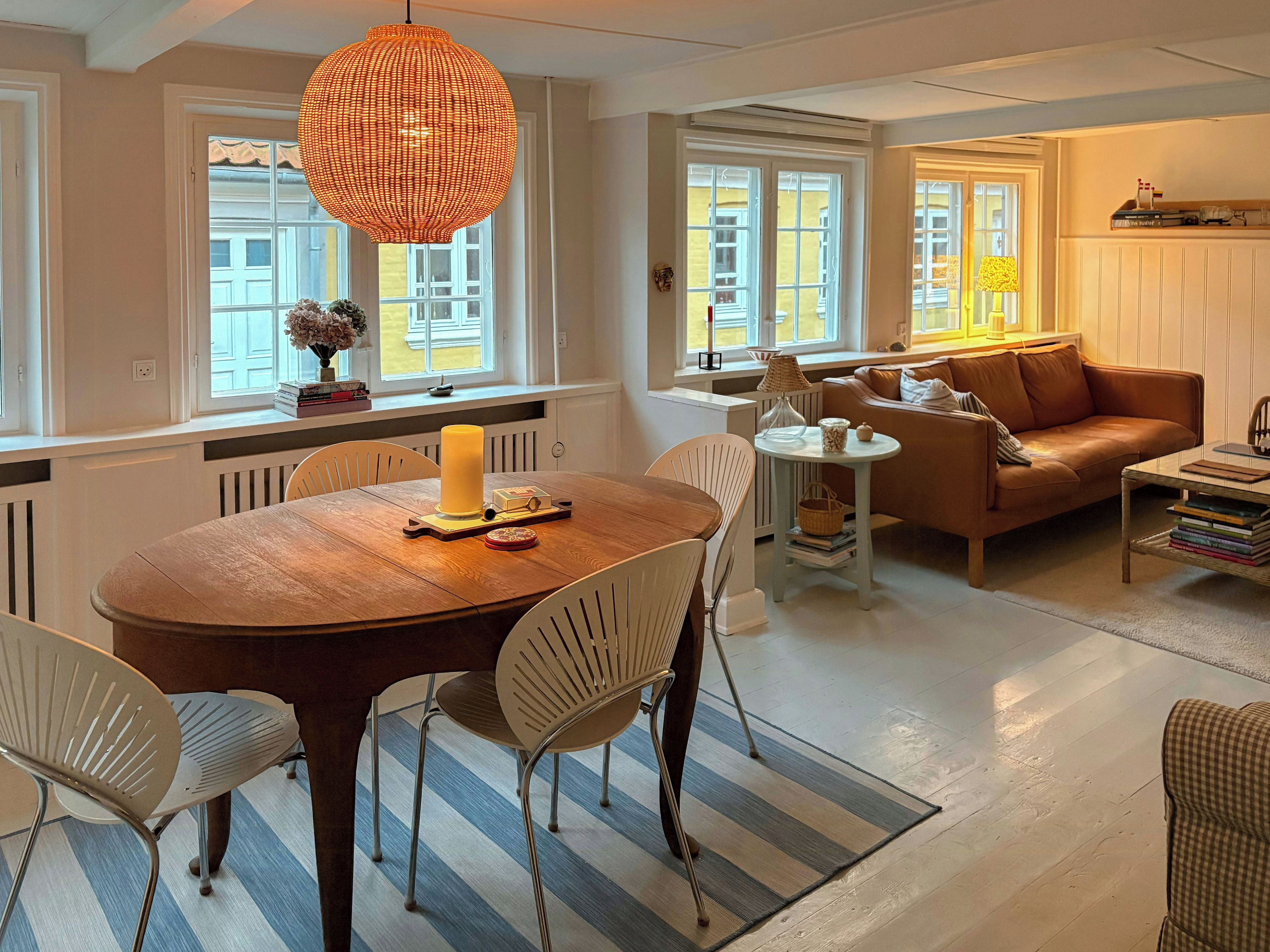 A dining area with a wooden table, chairs, a candle, and a hanging light fixture.