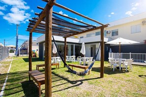 An outdoor patio area with a wooden pergola, white plastic chairs, a hammock, and a table. - Apt. in Condo. w/ Pool nr. 700m Beach Pcb0106 (Santa Cruz Cabralia)
