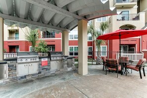 An outdoor patio with a barbecue grill, seating area, and a covered section. - Landing Chic 1bd, Courtyard (Houston)
