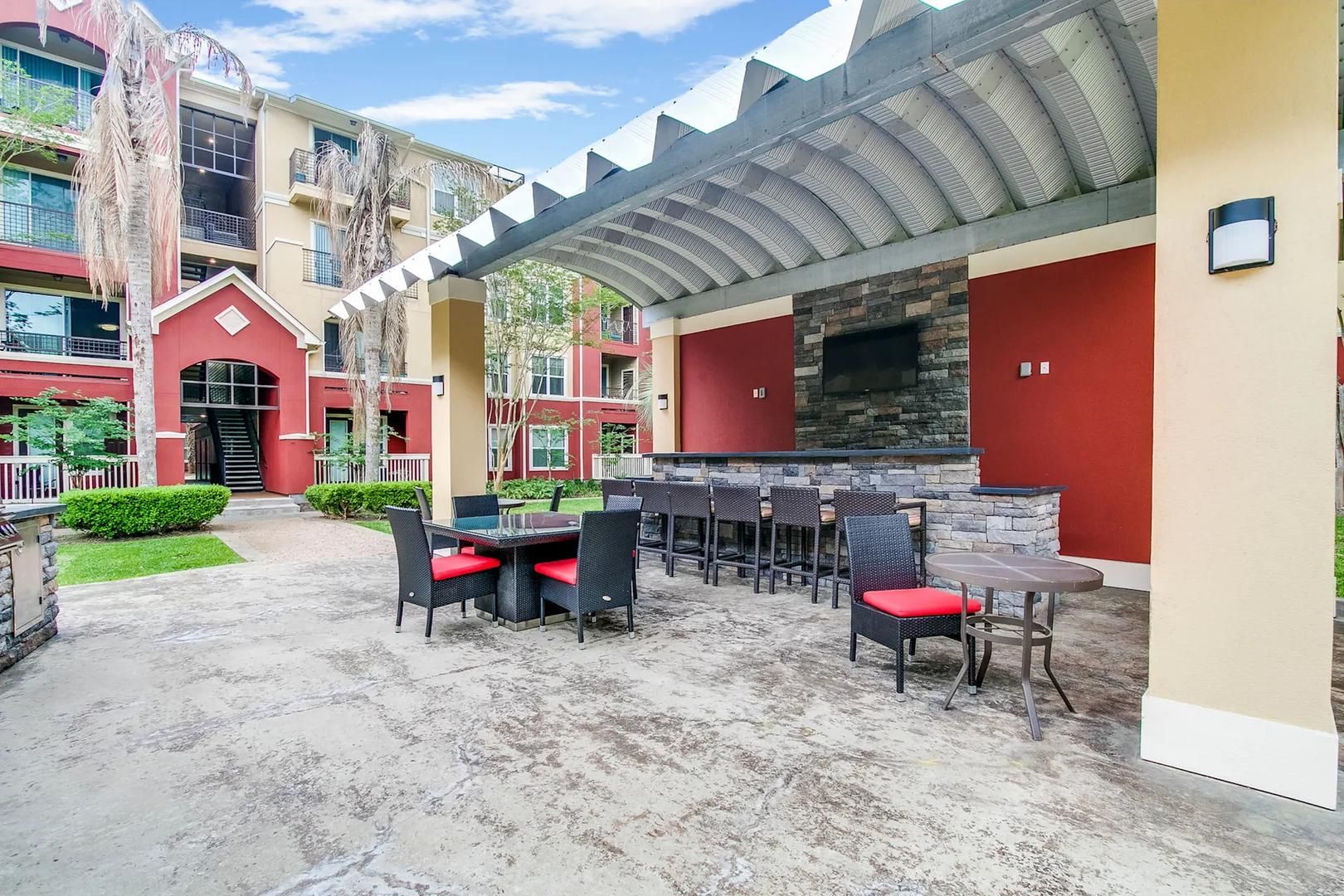 An outdoor patio area with a stone fireplace, multiple seating arrangements, and a covered walkway.