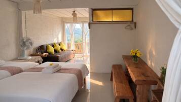 A bedroom with two beds, a wooden bench, a table with flowers, and a fan.