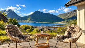 Two wicker chairs with fur throws on a wooden deck overlooking a mountainous landscape and a body of water. - Unique Lofoten Cabin with Spectacular Ocean Views and Sauna (Nordland)