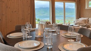 Une table à manger dressée pour six personnes, avec assiettes, verres et une carafe, donnant sur un paysage pittoresque.