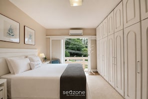 Ein Schlafzimmer mit Bett, Nachttisch, Lampe, Kleiderschrank und Blick ins Freie.