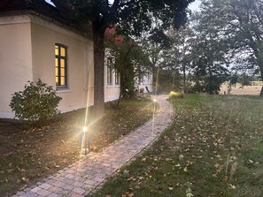 A pathway leading to a building with a window, surrounded by grass and trees. - Cozy 2-room apartment for a relaxing getaway (Müden (Aller))