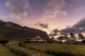 Une maison moderne avec un toit plat, entourée d’une pelouse bien entretenue et avec une grande montagne en toile de fond.